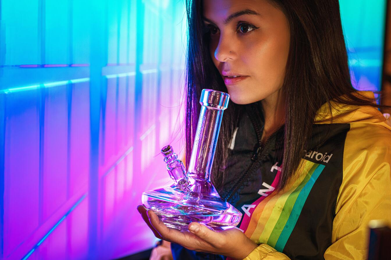 young woman smoking bong near neon-colored wall